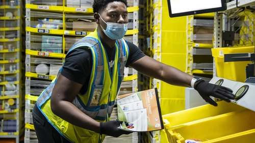 Работник склада Amazon берёт предмет из контейнера и кладёт его в ящик на роботизированном складе